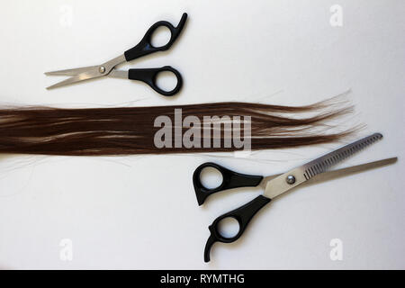 Zwei Paare von friseurscheren mit einem Schloss von Auburn brünette Haare. Schneid- und Modellierschere neben langen reddy braunes Haar Stockfoto