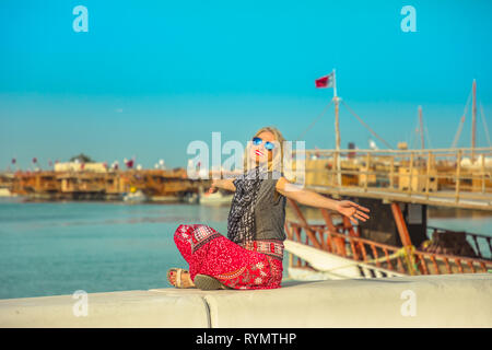 Tourismus in Katar. Happy kaukasische Frau genießen, entlang der Corniche mit Dhow Hafen für den Hintergrund. Lifestyle Touristen in der Stadt Doha, Katar Stockfoto