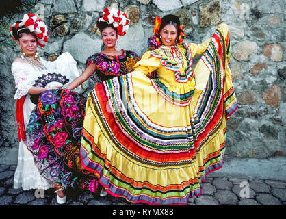 Drei lächelnd weibliche folkloristische Tänzer zeigen ihre wunderschönen traditionellen Kleider von verschiedenen Stoffen und Designs vor der Durchführung für Touristen in einem Resort in Acapulco an der Pazifikküste von Mexiko, Nordamerika. Stockfoto