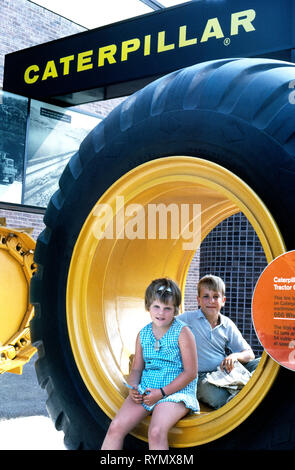 Zwei junge messebesucher Rest in der Nabe eines riesigen 10 Fuß - hoch (3 Meter) Gummi Traktor Reifen vor der Caterpillar Ausstellung am 1964-65 in New York World's Fair in Flushing Meadows Park im Stadtteil Queens, New York, USA. Cat ist der weltweit führende Hersteller von Bau- und Bergbaumaschinen, und fast 200 ihrer Erdbewegungsmaschinen wurden in den Bau der 646 Hektar (261 Hektar) Messegelände verwendet. Amerikanische Unternehmen anstatt Länder aus der ganzen Welt waren die großen Aussteller auf dieser größten der Weltausstellungen, die jemals in den Vereinigten Staaten gehalten. Stockfoto