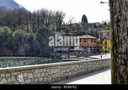 Mergozzo, Piemont, Italien. März 2019. Blick auf den Beginn der Lakeside am Fuße des Hügels. Ein Pub mit Blick auf den Yachthafen, wo die kleinen Boote Stockfoto