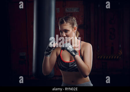 Junge weibliche Kämpfer werfen eine Aufregung der Schläge auf die schwere Tasche Bewegungsunschärfe auf ihre Hände. MMA sportliche Frau Stockfoto