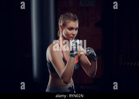 Junge weibliche Kämpfer werfen eine Aufregung der Schläge auf die schwere Tasche Bewegungsunschärfe auf ihre Hände. MMA sportliche Frau Stockfoto