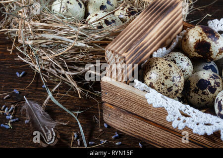 Wachteleier immer noch Leben. Wachteleier liegen in einem Nest aus Heu und in einem hölzernen Kasten auf einer Spitze Serviette. Close-up Stockfoto