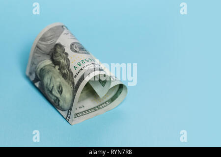 Geld Geschenk und kommerzielle Geldanlage gewinn Konzept. US Dollar 100 Hinweis Herzform auf leeren blauen Hintergrund Stockfoto