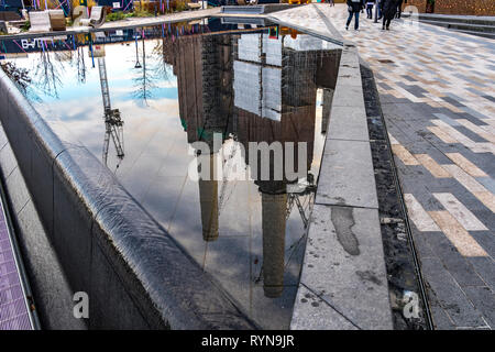 Die Kamine des Battersea Power-Kraftwerks spiegeln sich in einem Wasserspiel im Circus West Village, Battersea, London, Großbritannien, wider Stockfoto