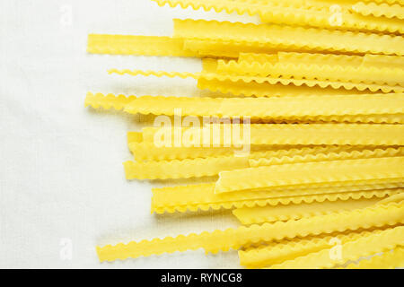 Raw italienische Pasta genannt mafaldine auf weißem Baumwollstoff, flache und breite Nudeln mit welligen Kanten auf beiden Seiten Stockfoto
