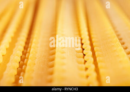 Raw italienische Pasta genannt Mafaldine, flache und breite Nudeln mit welligen Kanten auf beiden Seiten, schöne abstrakte Wirkung, Makro Fotografie Stockfoto