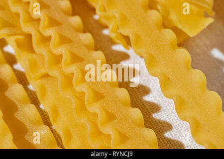 Raw italienische Pasta genannt mafaldine auf weißem Baumwollstoff, flache und breite Nudeln mit welligen Kanten auf beiden Seiten, schöne Schatten im Hintergrund Stockfoto