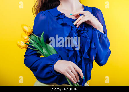 Studio Schoß einer Frau tragen Feder Outfit und Holding gelbe Tulpen auf gelbem Hintergrund Stockfoto