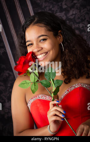 Eine schöne, biracial High School älteres Mädchen mit roten Kleid mit einer roten Rose Stockfoto