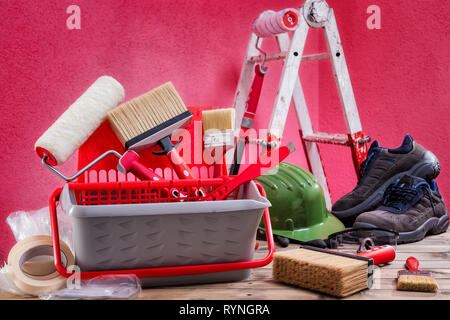 Professionelle Maler Werkzeuge. Bürsten, Walze, Behälter, Kunststoff- und Schutzfolie auf einen alten Holztisch. Bauindustrie. B Stockfoto