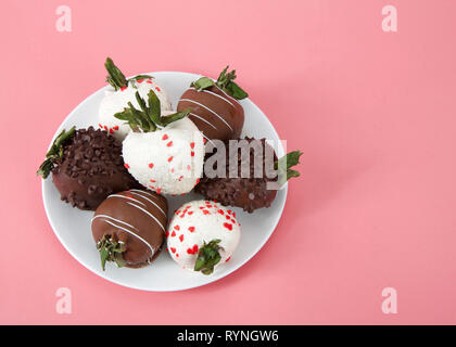 Vielzahl von mit Schokolade überzogene Erdbeeren auf einem Teller. Dunkle, Weiß und Milch Schokolade auf einem rosa Hintergrund. Ansicht von oben. Stockfoto