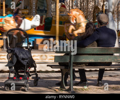 Paar in der Nähe des Karussells auf der Bank sitzen warten auf ein Kind reitet Karussell. Stockfoto