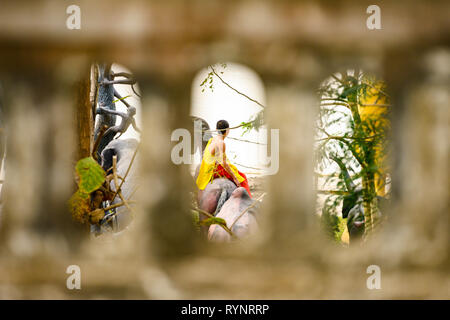 Ein buddhistischer Mönch, der von einer Mauer mit Bögen umrahmt wird, sitzend auf einem Pferd, Skulptur in Luang Prabang, Laos. Stockfoto