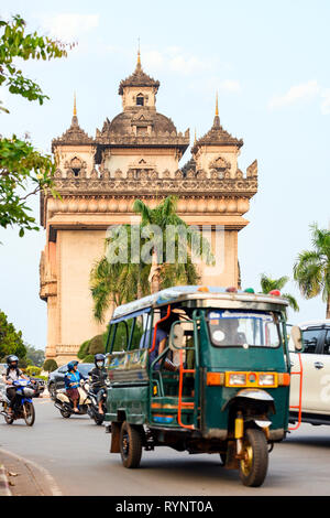 Atemberaubende Aussicht auf die schöne Patuxai mit Autos, Motorräder und einen traditionellen Tuc Tuc (Auto-rikscha) im Vordergrund. Vientiane, Laos. Stockfoto