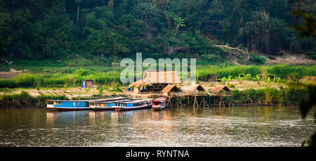 Wunderschöne traditionelle Hütten mit grünen Feldern in den Hintergrund und die Boote aus Holz auf dem Mekong Fluss verankert. Stockfoto