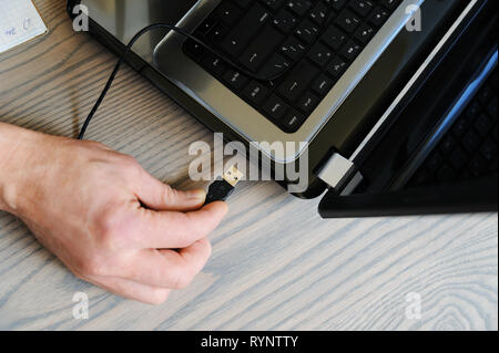 Die Hand des Menschen verbindet das USB-Kabel mit dem Laptop. Ansicht von oben. Stockfoto