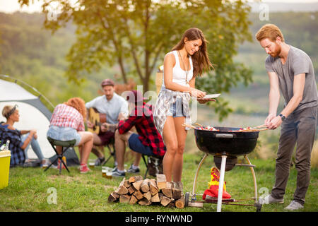 Junge brünette Mädchen mit Freund, Grill Fleisch im Grill in Campground Stockfoto