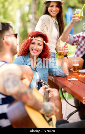 Junge glücklich Curly rothaarigen Mädchen Toasts mit hipster Kerl mit Gitarre außerhalb Stockfoto