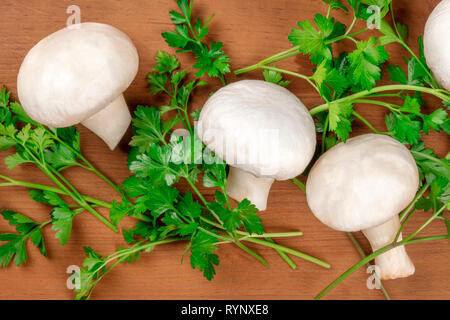 Champignon Pilze, geschossen von oben auf einen rustikalen Holzmöbeln Hintergrund mit frischer Petersilie Stockfoto