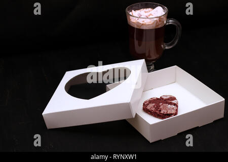 Hot Drink in ein Glas Schale mit rosa Marshmallows und White Box mit transparentem Deckel in der Form von Herzen mit Cookies Stockfoto