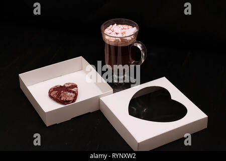 Hot Drink in ein Glas Schale mit rosa Marshmallows und White Box mit transparentem Deckel in der Form von Herzen mit Cookies Stockfoto