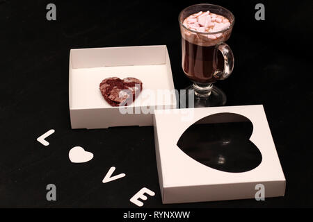 Hot Drink in ein Glas Schale mit rosa Marshmallows und White Box mit transparentem Deckel in der Form von Herzen mit Cookies Stockfoto