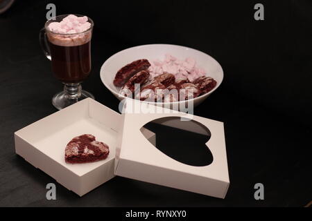 Hot Drink in ein Glas Schale mit rosa Marshmallows und White Box mit transparentem Deckel in der Form von Herzen mit Cookies Stockfoto