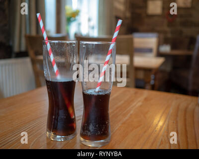 Zwei Getränke Gläser mit streifiger Papier Trinkhalme auf einer hölzernen cafe Tabelle Stockfoto