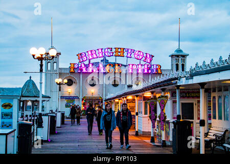 Menschen flanieren auf Brighton Palace Pier am Abend mit seinen bunten Zeichen in der gedimmtem Licht glühenden Stockfoto