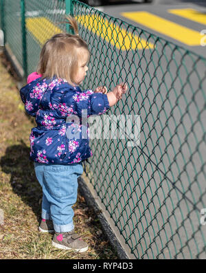 Süße 17-Monate altes Baby Mädchen schauen durch die Meral Zaun. Outdoor und Leiter Fotografie Stockfoto