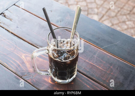 Vietnamesische kalten Kaffee mit Eis in einem Becher mit einem Löffel und einem Stroh auf den Holztisch. In einem Straßencafe, für 10 000 Dong (0,4 $). Stockfoto