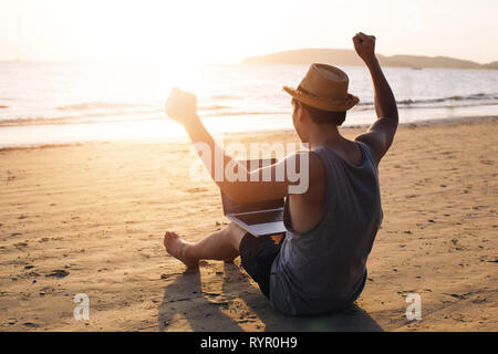 Junge männliche Geschäftsmann Hände hoch setzend für Erfolg auf tropischen Sommer Strand - es zeigt an, dass die Freiheit wie finanzielle Freiheit oder remote arbeiten Konzept. Stockfoto