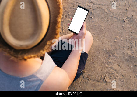 In der Nähe von jungen männlichen Reisenden mit Handy mit leeren weißen Bildschirm am tropischen Strand - mit Kopie Raum und Freistellungsmaske eine adverti einfügen Stockfoto