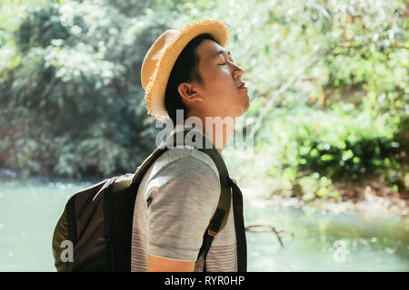 Jungen Asiatischen männlichen Reisenden genießen und inhalieren gesunde Luft in grüner Natur Wald - frische Luft und Leben Wohlbefinden. Stockfoto