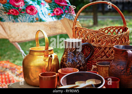Still-Leben mit Kupfer Wasserkocher und vintage Steingut, Weidenkorb. Bemalten Tuch und grünes Gras im Hintergrund Stockfoto
