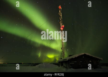 Ein Ferienhaus und Fernsehturm im Vordergrund und Aurora Borealis (Nordlicht) im Abstand hinter oben Ivalo in Nord Lappland. Saariselka, Stockfoto