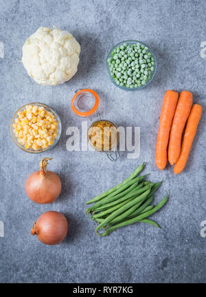 Zutaten für Zwiebel Currypaste auf hellgrauem Hintergrund. Bild von zwei Zwiebeln, Blumenkohl, Erbsen, Mais, Bohnen und Karotten auf grauem Hintergrund Stockfoto