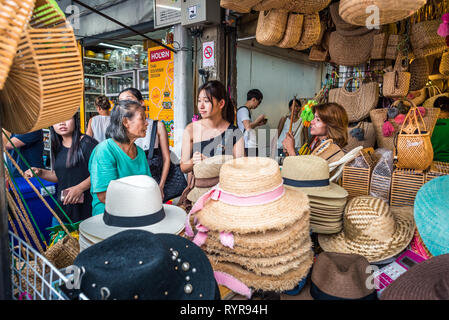 Bangkok, Thailand - 13. Mai 2018: Drei Frauen miteinander reden hinter einer Ladentheke mit Hüten und Korbwaren Taschen bei Chatuchak Weekend Market gefüllt. Stockfoto