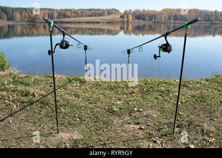 Zwei karpfenruten sind auf steht am Ufer gegen die flache Oberfläche der See installiert. Hintergrund. Stockfoto