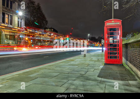 London, England, 14. März 2019. Eine berühmte rote Telefonzelle in der Stadt neben einer viel befahrenen Straße mit leichten Wanderwegen bei Nacht Stockfoto