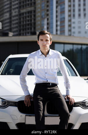 Jungen gutaussehenden Mann im Hemd in der Nähe der weißen Auto. Konzept der erfolgreichen Stockfoto