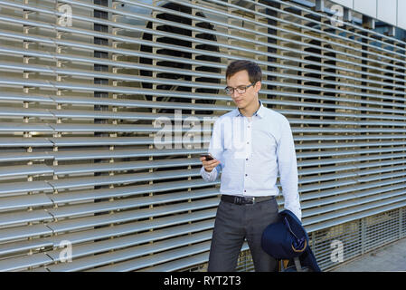 Jungen gutaussehenden Mann Geschäftsmann mit Brille in Shirt. Freiberufler ist Telefon Holding. Konzept der erfolgreichen Stockfoto
