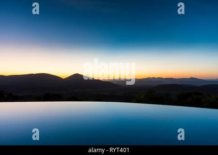 Swimmingpool über schönen Ausblick mit Blick auf die Berge bei Sonnenuntergang, Ovapu, Kaokoveld, Namibia Stockfoto