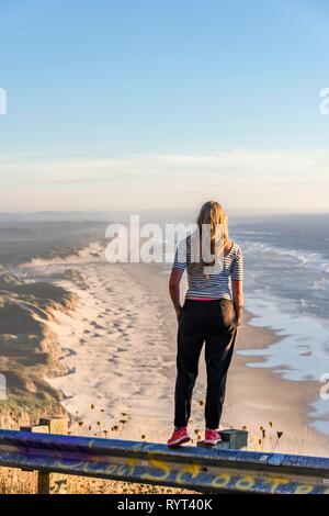 Junge Frau in die Ferne an einem Aussichtspunkt, mit Blick auf Baker Beach mit langen Sandstrand suchen, Oregon Coast Highway, Oregon Stockfoto