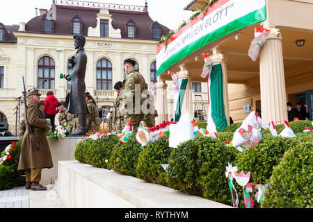 Sopron, Ungarn. 15 Mär, 2019. Soldaten der "honvéd Hagyományőrző Egyesület" stehen rund um die Statue des ungarischen Dichters Sándor Petőfi bei Petőfi Square, Sopron, Ungarn. Ungarische Symbole, Flaggen, die von den Kindern in buxus Pflanzen im Vordergrund blockiert. Credit: Wahavi/Alamy leben Nachrichten Stockfoto