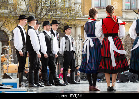 Sopron, Ungarn. 15 Mär, 2019. Eine Gruppe von Volkstänzer Jungs stehen und singen auf der Bühne des Petőfi Square, Sopron, Ungarn. Mädchen in Tracht stehen auf der rechten Seite. Credit: Wahavi/Alamy leben Nachrichten Stockfoto