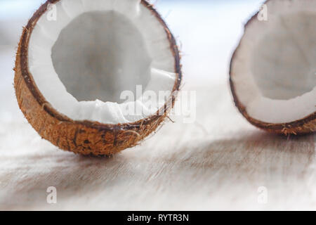 Zwei Hälften der Kokosnuss auf einem hellen weißen Holz- Hintergrund, close-up. Blick von oben. Stockfoto