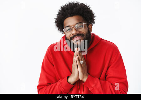 Chillen und unbeschwerte freundlich aussehende afrikanischer amerikanischer Mann mit Bart in Gläsern, Engel aussehen, als Hände halten in beten und bitten um Gnade oder Stockfoto